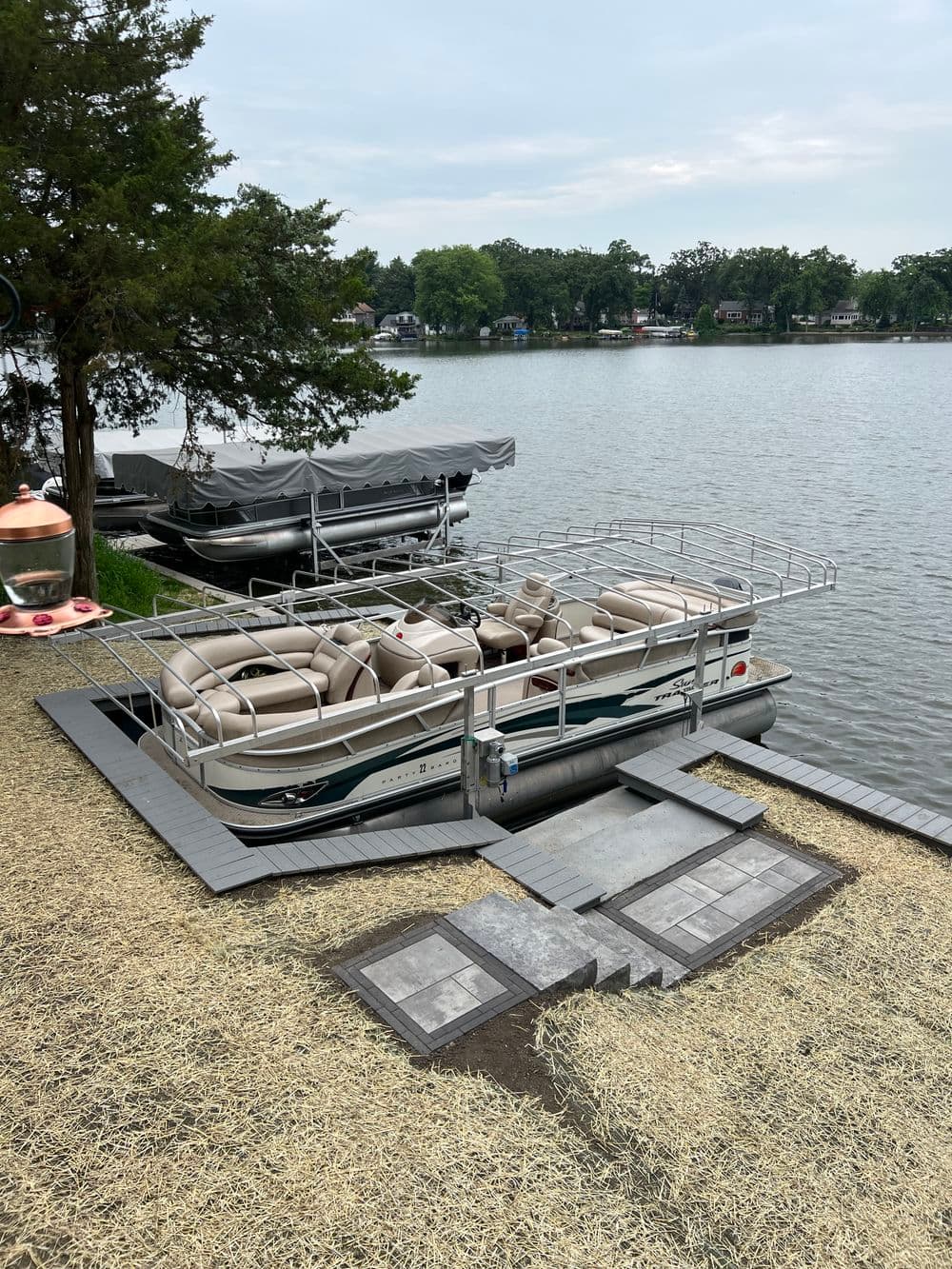 Pontoon boat on a dock by the lake, surrounded by trees and adjacent boats.