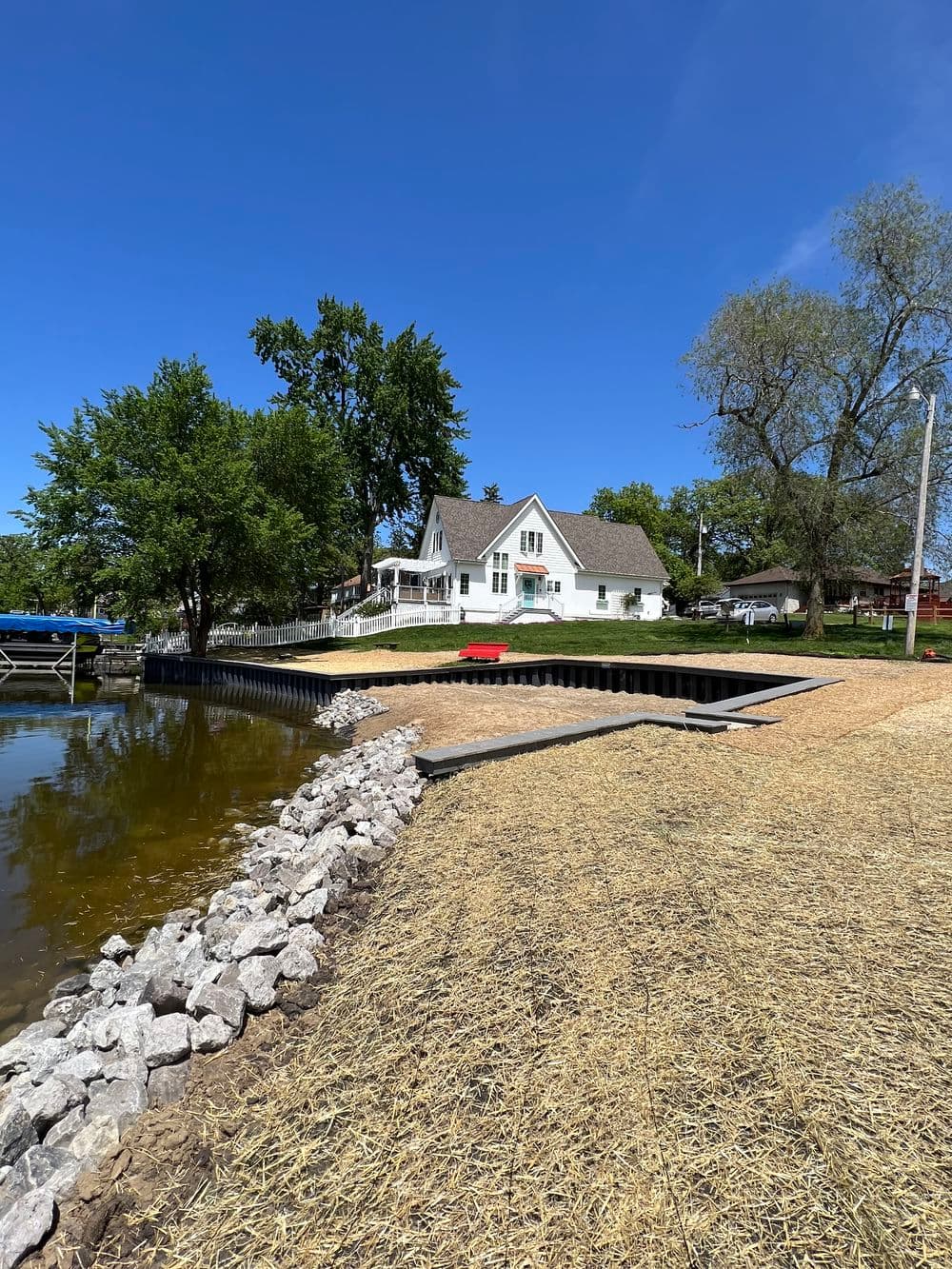 Lakeside property with a house, dock, and sandy beach under a clear blue sky.
