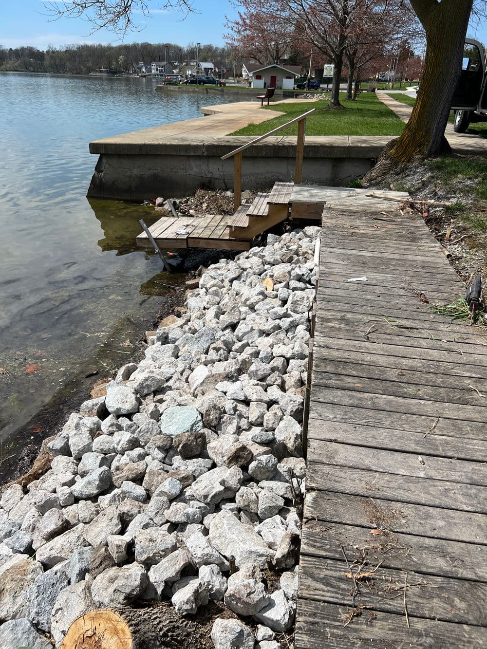 Dock and rocky shore along a calm lake, with trees and benches in the background.