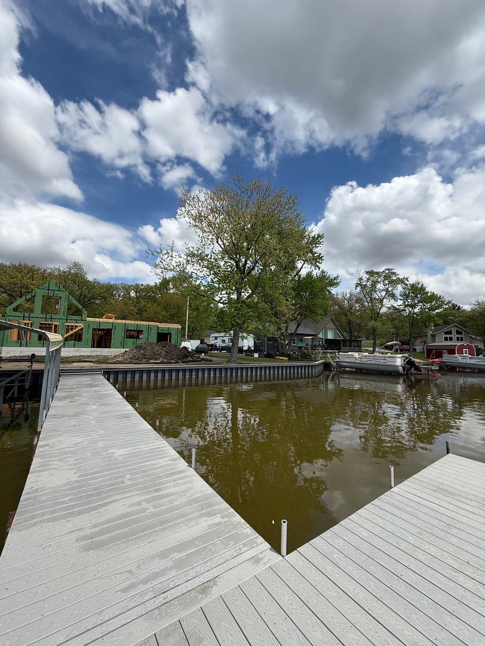 Calm waterfront scene with a tree, docks, and cloudy sky reflecting in the water.