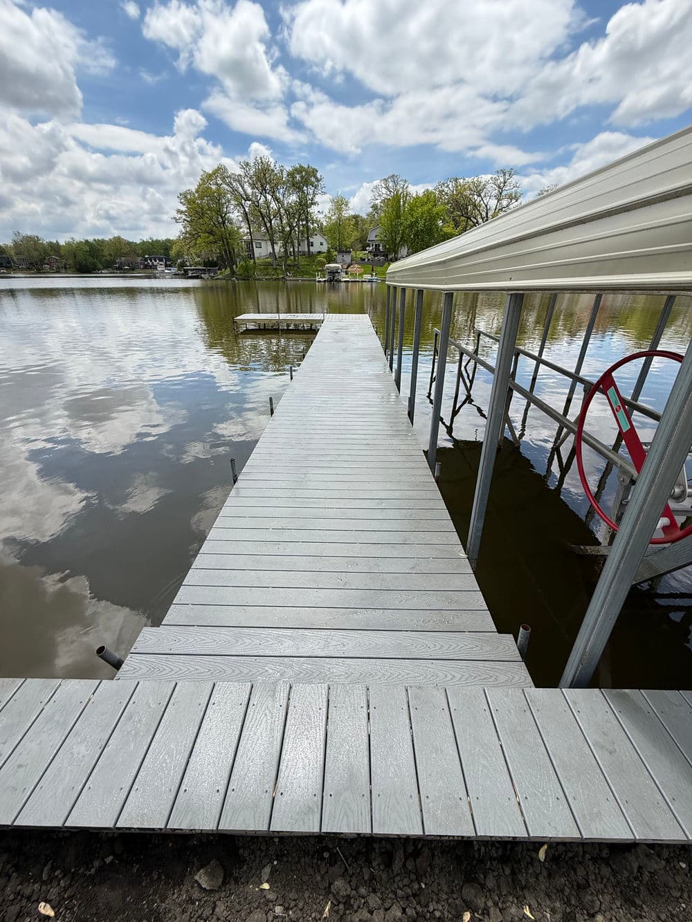 Dock extending over calm water, surrounded by trees and a cloudy sky. Ideal for boating or relaxation.