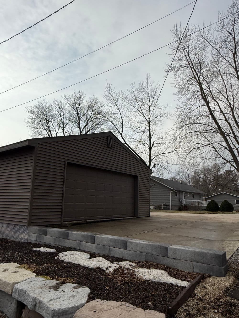 Modern brown garage with a concrete driveway and leafless trees in the background.
